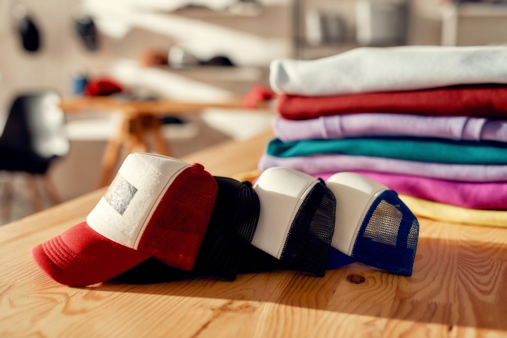 Custom apparel, clothes neatly folded on shelves. Stack of colorful clothing and baseball caps in the store. Horizontal shot. Selective focus